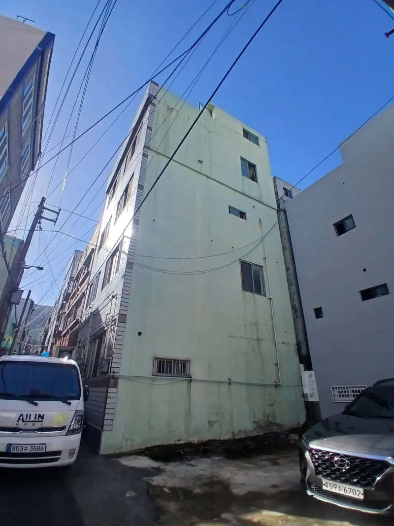 좁은 골목에서 올려다본 연두색 외벽의 4층 건물과 주차된 차