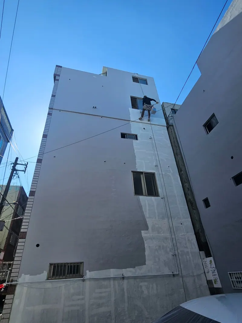 위층부터 회색으로 칠해지고 있는 외벽과 꼭대기 근처의 작업자