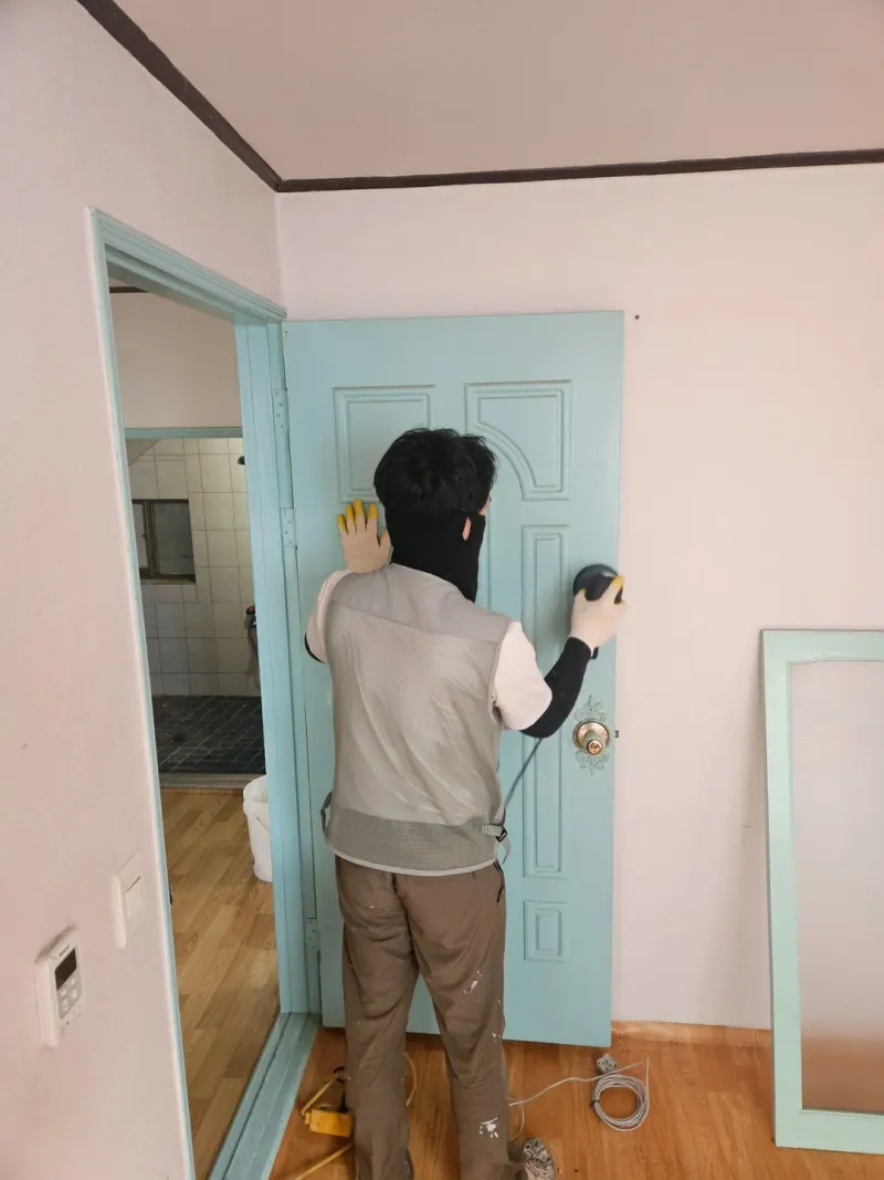 민트색 실내 문을 칠하는 작업자의 뒷모습.
